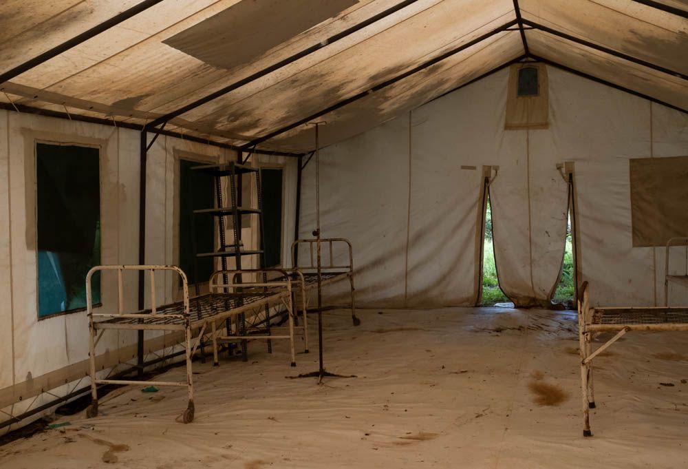 Empty metal bed frames stand inside a canvas clinic tent.