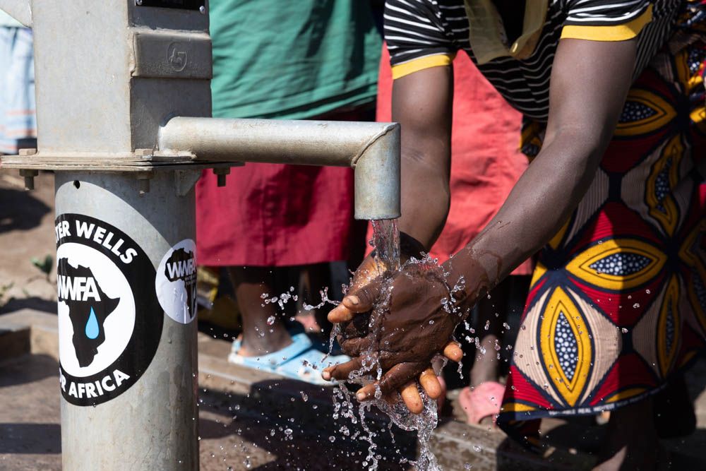 Hands catch water from a Water Wells for Africa hand pump.