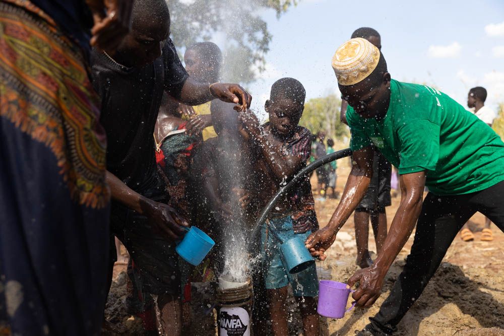 People hold out cups as water bursts from a newly drilled borehole.